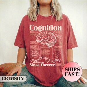 May include: Crimson t-shirt featuring the word "Cognition" and a detailed brain diagram in white. The shirt also displays the phrase "Overthinking Since Forever!" and a "Ships Fast!" sticker.