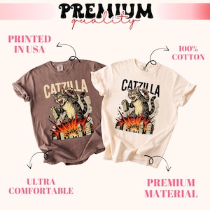 May include: Two t-shirts, one brown and one cream, feature a graphic of a cat labeled "CATZILLA" destroying a city. The shirts are labeled "Printed in USA", "Ultra Comfortable", "100% Cotton", and "Premium Material".
