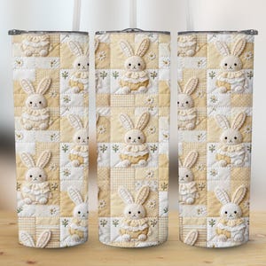 Op de afbeelding: Drie roestvrijstalen bekers met een herhalend patroon van een konijnenquiltdesign. Het ontwerp heeft een patchwork van gele en witte vierkanten met geborduurde konijnenfiguren en bloemaccenten. Elke beker heeft een wit rietje.