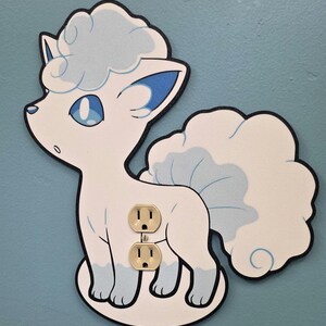 May include: A decorative wall plate cover shaped like a white and light blue fox-like creature with a large, fluffy tail. The cutout features a central opening for a standard two-socket electrical outlet, with the beige outlet visible through it.