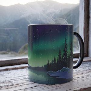 May include: A black coffee mug with a colorful aurora borealis scene and a silhouette of a forest reflected in a lake. The mug has a black handle.