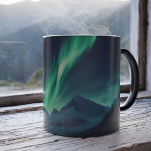 May include: A black coffee mug with a colorful image of the aurora borealis over a mountain range. The mug is sitting on a wooden surface.