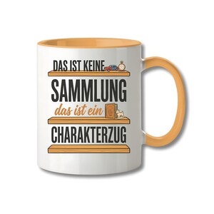 May include: A white ceramic mug with an orange interior and handle. The front features three horizontal wooden shelves with the German text "DAS IST KEINE SAMMLUNG das ist ein CHARAKTERZUG" and small illustrations of a car, clock, book, and dog.