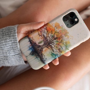 May include: A watercolor painting of a tree with colorful leaves on a white phone case. The case has a speckled background and a camera cutout.