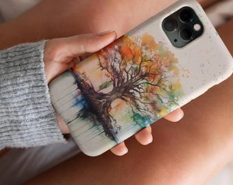 May include: A watercolor painting of a tree with colorful leaves on a white phone case. The case has a speckled background and a camera cutout.