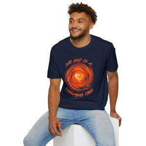 May include: Navy blue t-shirt featuring a fiery heart design at the center of a swirling orange and red graphic. The text "OUR GOD IS A CONSUMING FIRE" is arched above and below the design. The shirt is made of a soft material.