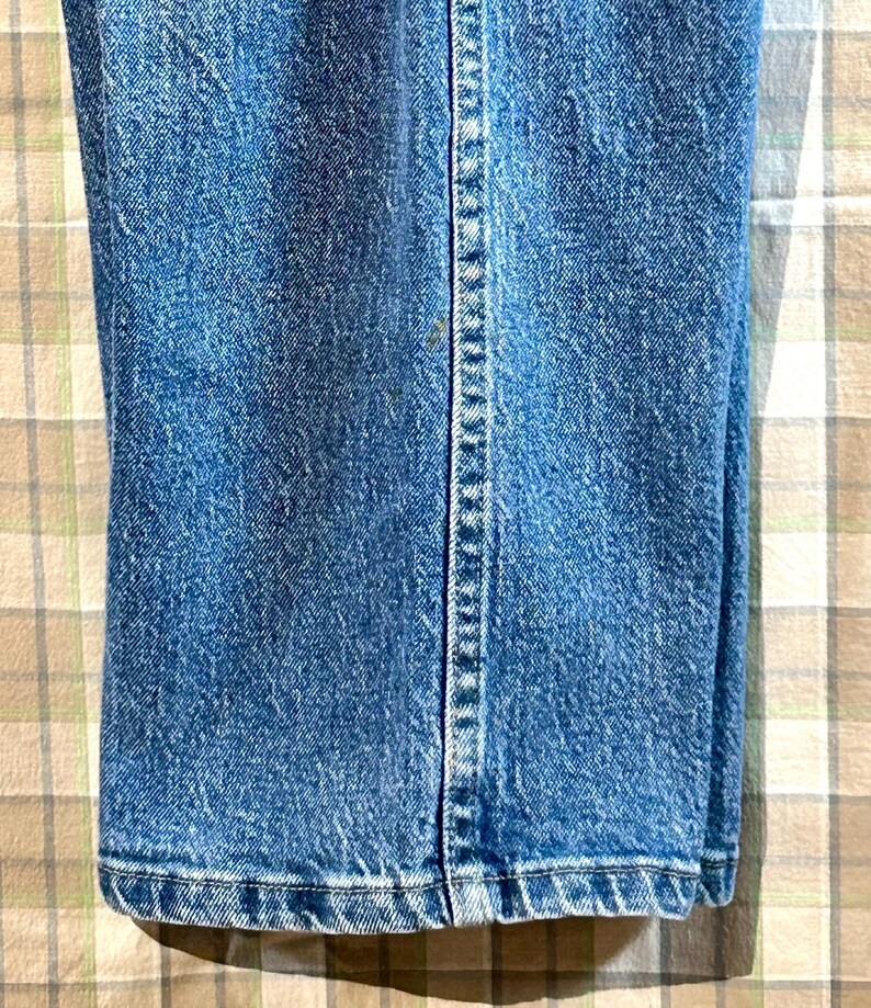K&ouml;nnte beinhalten: Nahaufnahme des unteren Saums einer blauen Jeans. Die Jeans hat einen geraden Schnitt und eine klassische Passform.