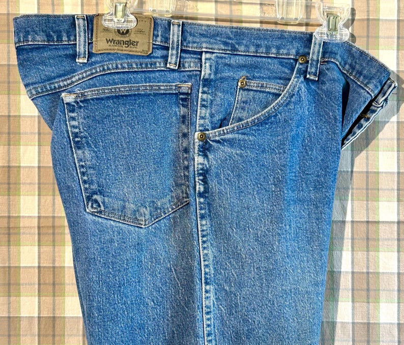 K&ouml;nnte beinhalten: Eine blaue Jeanshose mit einem braunen Leder-Patch auf der Ges&auml;&szlig;tasche, auf dem "Wrangler" steht.