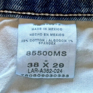 K&ouml;nnte beinhalten: Ein wei&szlig;es Etikett mit schwarzem Text, das angibt, dass die Jeans in Mexiko hergestellt wurden. Das Etikett enth&auml;lt auch die Gr&ouml;&szlig;e, 38 x 29, und die Artikelnummer 85500MS. Das Etikett ist an einer blauen Jeans aus Denim befestigt.