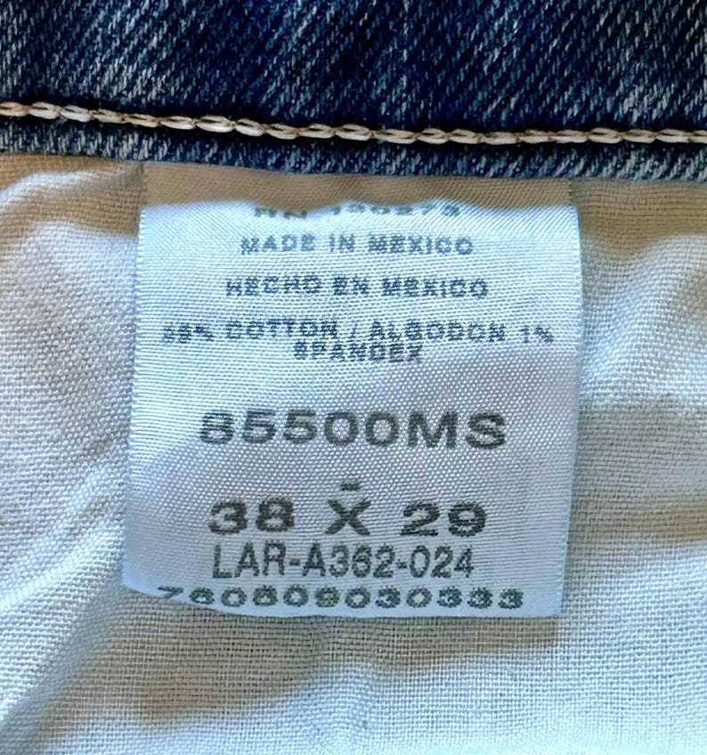 K&ouml;nnte beinhalten: Ein wei&szlig;es Etikett mit schwarzem Text, das angibt, dass die Jeans in Mexiko hergestellt wurden. Das Etikett enth&auml;lt auch die Gr&ouml;&szlig;e, 38 x 29, und die Artikelnummer 85500MS. Das Etikett ist an einer blauen Jeans aus Denim befestigt.