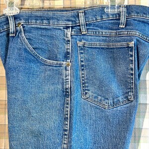 K&ouml;nnte beinhalten: Eine blaue Jeanshose mit einer einzigen Ges&auml;&szlig;tasche und einem Knopfverschluss.