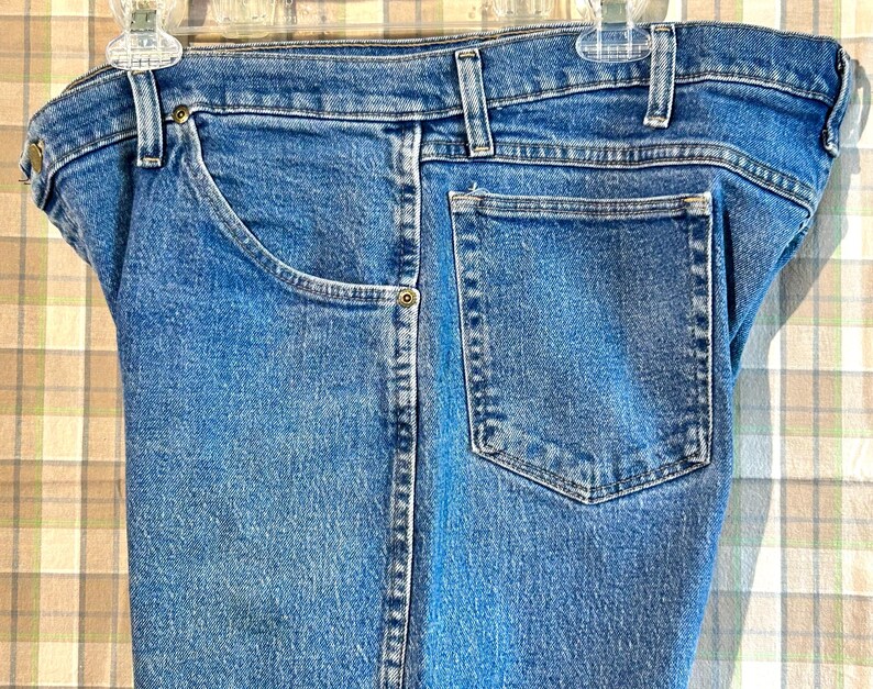 K&ouml;nnte beinhalten: Eine blaue Jeanshose mit einer einzigen Ges&auml;&szlig;tasche und einem Knopfverschluss.