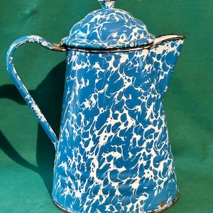 Puede incluir: Cafetera vintage de esmalte azul y blanco. Presenta un patrón de remolino blanco sobre fondo azul. Cuenta con un asa curvada y un pico vertedor. Un objeto de cocina con encanto para servir café o té.