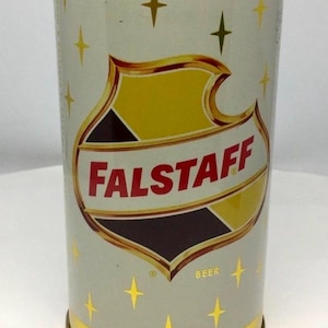 May include: Vintage Falstaff beer can with a gold rim and base. The can is light gray with a shield-shaped logo in yellow, brown, and white, and the word "Falstaff" in red. Gold starbursts are scattered across the can.