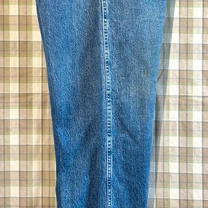 K&ouml;nnte beinhalten: Eine blaue Jeanshose mit einem braunen Leder-Wrangler-Etikett auf der Ges&auml;&szlig;tasche.