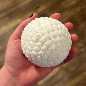May include: A white, fluffy, round ball, resembling a snowball, is held in a person's hand.
