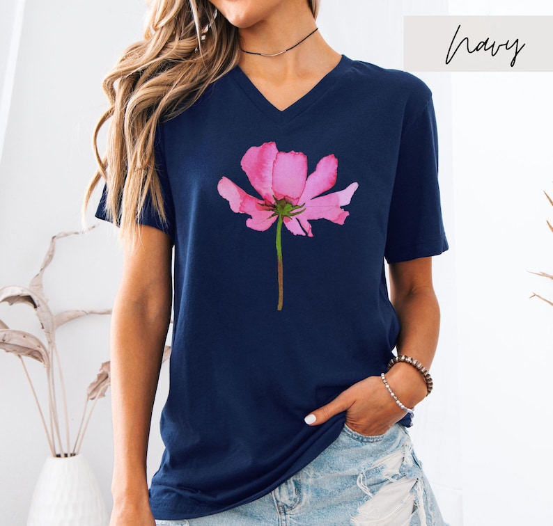 May include: A navy blue t-shirt with a pink watercolor flower graphic. The shirt has a v-neck and short sleeves.