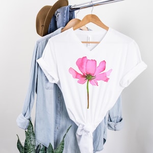 May include: White t-shirt with a pink watercolor flower design.