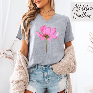 May include: Gray V-neck t-shirt with a pink watercolor flower graphic. The shirt is made of athletic heather fabric.