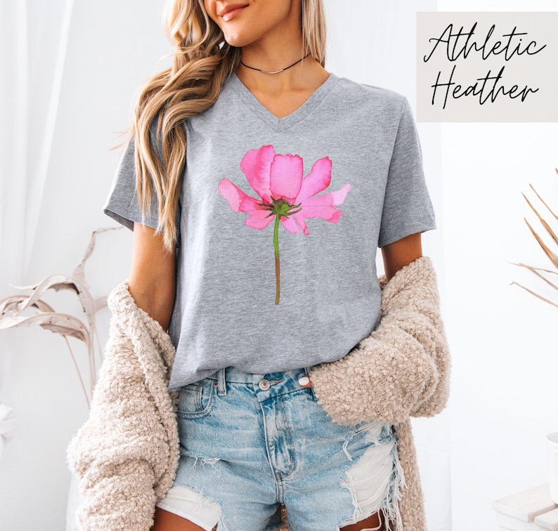 May include: Gray V-neck t-shirt with a pink watercolor flower graphic. The shirt is made of athletic heather fabric.
