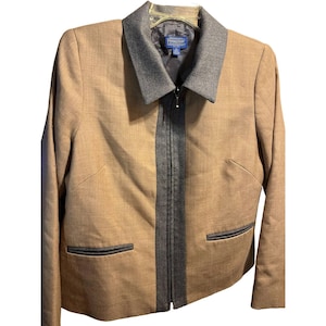Puede incluir: Chaqueta color beige con cuello gris y cremallera completa. La chaqueta tiene dos bolsillos delanteros con ribete gris y una franja gris en el centro. La marca "Pendleton" es visible en la etiqueta.