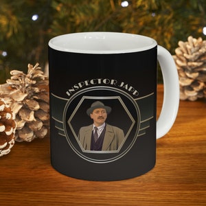 May include: A black and white mug with a gold design featuring a man in a hat and the text "INSPECTOR JAPP".