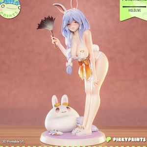 May include: A figurine of a female anime character with bunny ears, holding a feather duster. The character wears a white outfit with an orange bow. A white bunny figure is at the base. The text "Pekomama" and "HOLOLIVE" are visible.