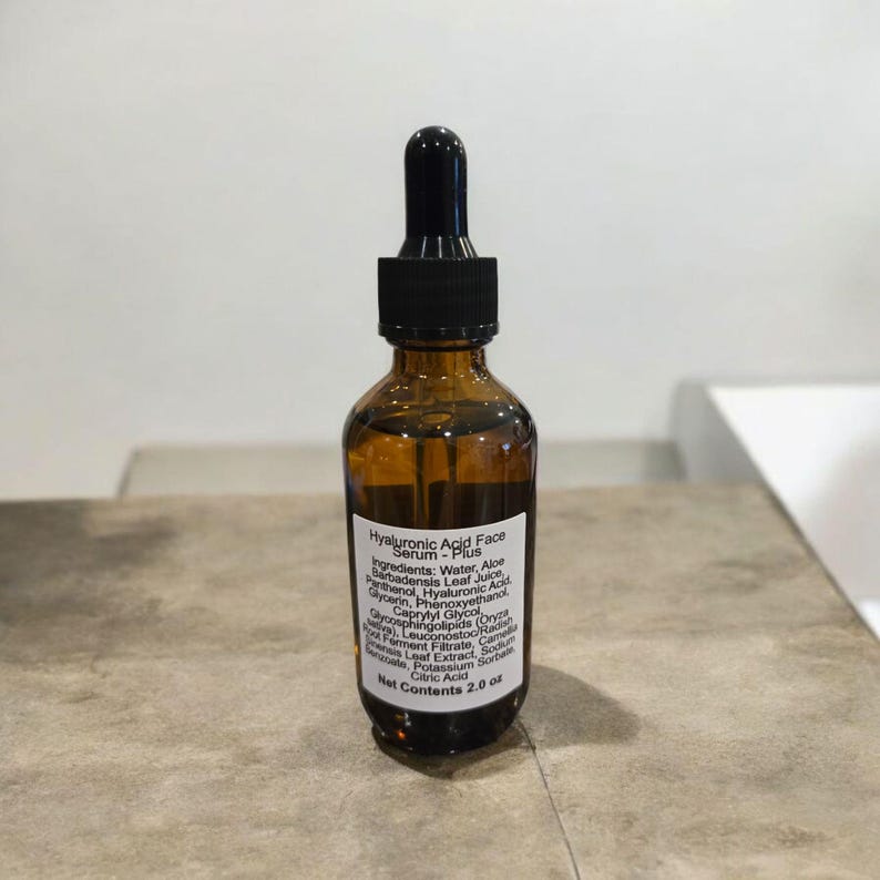 Peut inclure: Un flacon en verre brun avec un compte-gouttes noir. Le flacon est &eacute;tiquet&eacute; "Hyaluronic Acid Face Serum - Plus" et liste les ingr&eacute;dients. Le flacon contient 2,0 oz de s&eacute;rum.