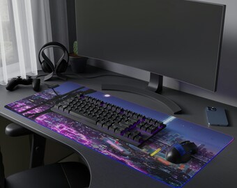 Könnte beinhalten: Ein schwarzer Computermonitor mit einem leeren Bildschirm steht auf einem Schreibtisch mit einer schwarzen Tastatur, einem lila und blauen Mauspad und einem schwarzen und weißen Telefon. Der Schreibtisch ist aus dunklem Holz.