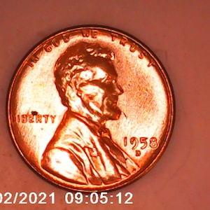 May include: A copper-colored 1958 Lincoln penny. The obverse features a profile of Abraham Lincoln, the word "LIBERTY", and the inscription "IN GOD WE TRUST". The date "1958" is visible. The coin is in good condition.