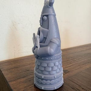 Op de afbeelding: Een grijs 3D-geprint beeldje van een krijger met een gehoornde helm die een bijl vasthoudt. Het figuur heeft een getextureerde tuniek met schubbenpatroon, een riem met ronde noppen en een decoratieve band rond de basis, alles in mat grijs.