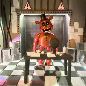 May include: A red bear figurine with a black top hat and bowtie stands behind a black desk. The desk holds papers, a small round object, and a cup. The scene features a checkered floor, two triangular warning signs, and stacks of grey boxes.