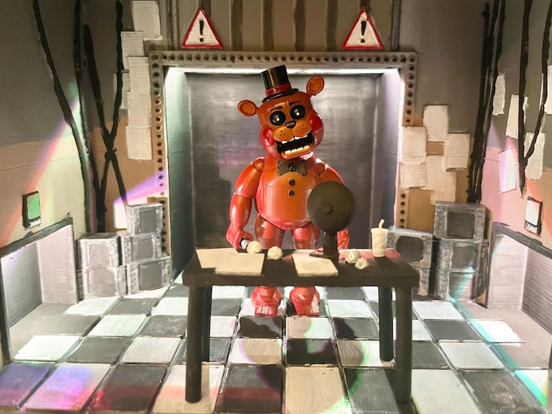 May include: A red bear figurine with a black top hat and bowtie stands behind a black desk. The desk holds papers, a small round object, and a cup. The scene features a checkered floor, two triangular warning signs, and stacks of grey boxes.