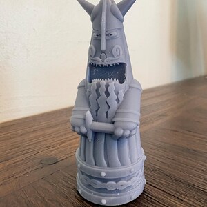 Op de afbeelding: Een lichtgrijs 3D-geprint beeldje van een gestileerde Viking-krijger met een gehoornde helm. Het figuur heeft een wijd open mond met zichtbare tanden, een lange golvende baard en handen die een klein zwaard voor de borst vasthouden.