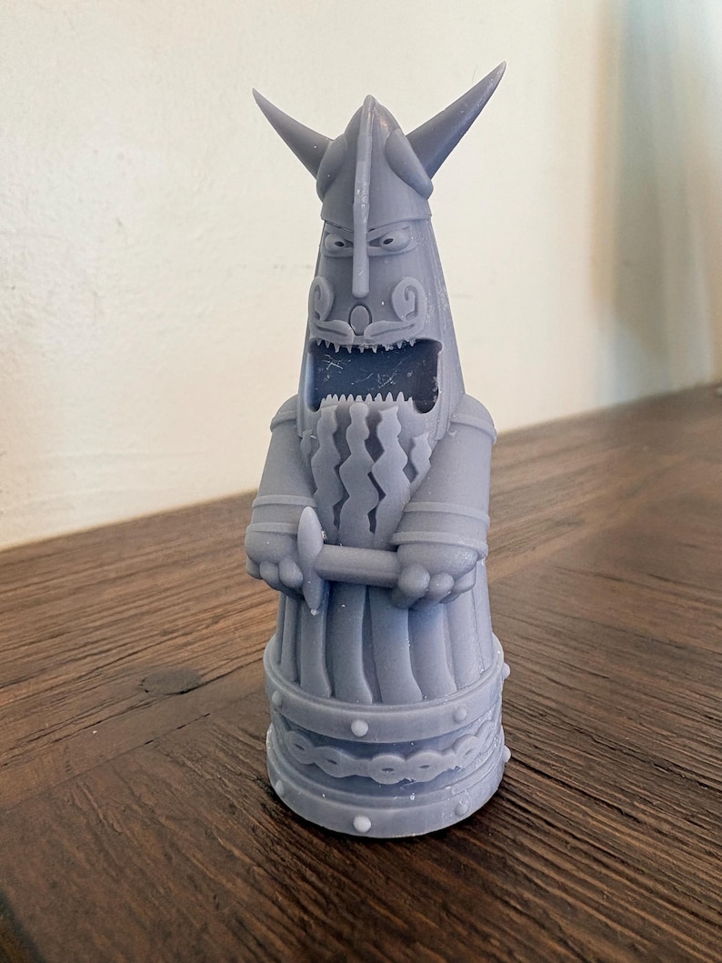 Op de afbeelding: Een lichtgrijs 3D-geprint beeldje van een gestileerde Viking-krijger met een gehoornde helm. Het figuur heeft een wijd open mond met zichtbare tanden, een lange golvende baard en handen die een klein zwaard voor de borst vasthouden.