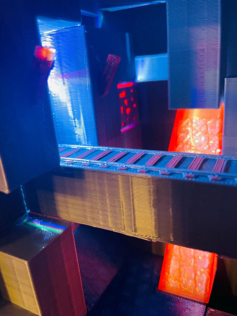 Puede incluir: Un modelo 3D impreso de una estructura futurista con un flujo de lava roja incandescente y una pasarela iluminada en azul. El modelo est&aacute; hecho de pl&aacute;stico y tiene una superficie texturizada.