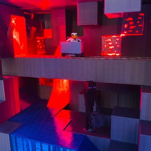 Puede incluir: Un diorama impreso en 3D con tem&aacute;tica de Minecraft con un esquema de iluminaci&oacute;n rojo y azul. Una peque&ntilde;a figura de un pollo montando un carro de minas est&aacute; en el nivel superior. Una figura de un personaje de piel negra con ojos morados est&aacute; en el nivel inferior.