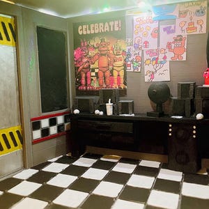 K&ouml;nnte beinhalten: Ein Miniatur-Diorama eines Sicherheitsb&uuml;ros mit schwarz-wei&szlig; kariertem Boden, einem Schreibtisch mit elektronischen Ger&auml;ten, einem Celebrate-Poster mit drei Figuren, Kinderzeichnungen an der Wand und einer T&uuml;r mit gelben Warnstreifen.