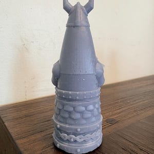 Op de afbeelding: Een lichtpaars, 3D-geprint beeldje van een krijger met een gehoornde helm. Het figuur heeft een gestructureerd, schubachtig patroon rond het middengedeelte, een riem met kleine noppen en een decoratieve band bij de basis. Het ontwerp is conisch.