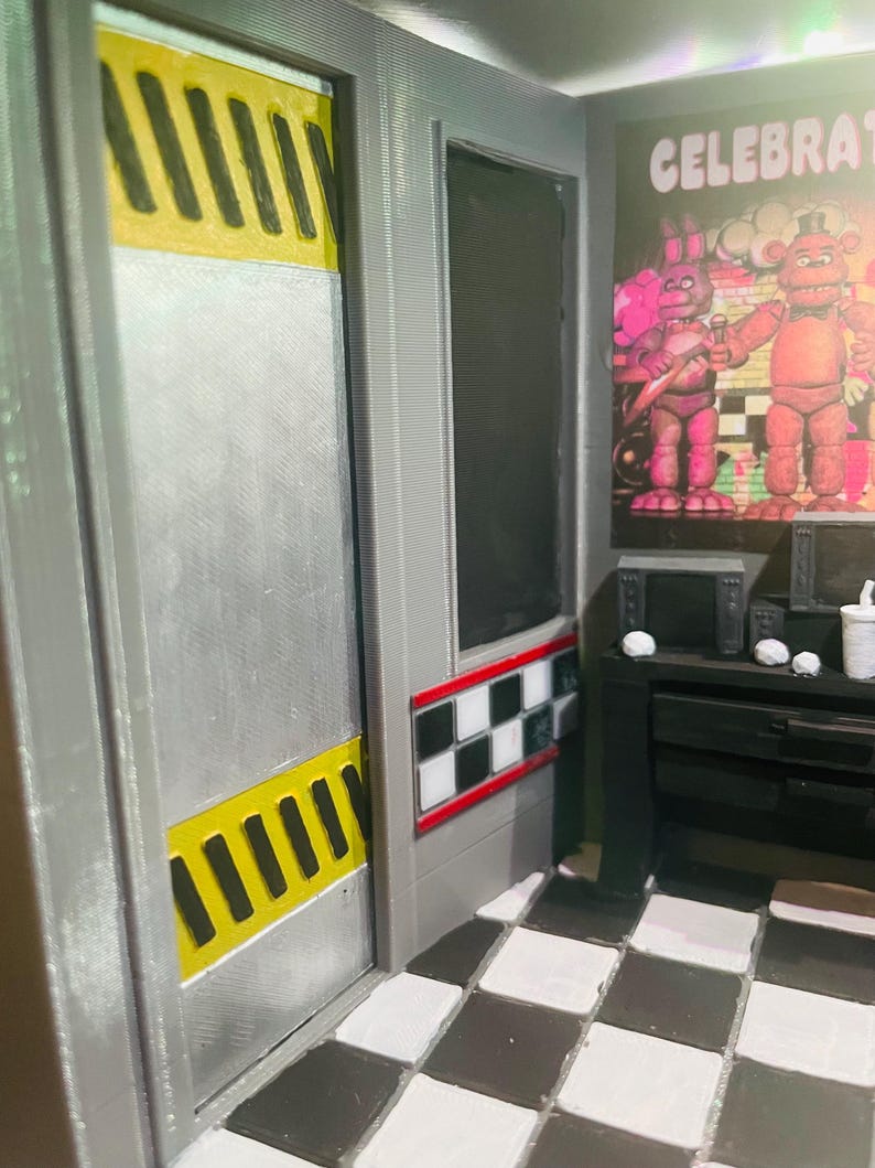 K&ouml;nnte beinhalten: Ein Miniatur-Diorama mit einer silbernen T&uuml;r mit gelb-schwarzen Warnstreifen, einem schwarz-wei&szlig; karierten Wandakzent und einem schwarz-wei&szlig; gefliesten Boden. Ein Poster zeigt zwei Zeichentrickfiguren mit dem Text CELEBRATE.
