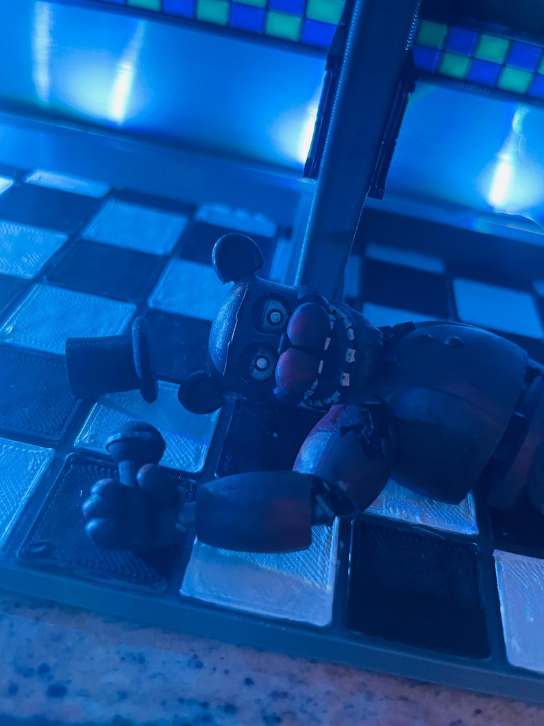 Op de afbeelding: Een donkerbruin berenfiguurtje met een hoge hoed, grote ogen en een zichtbaar kaakmechanisme, dat een kleine microfoon in &eacute;&eacute;n hand houdt. Het figuurtje heeft een versleten uiterlijk met zichtbare gewrichten op een geblokt oppervlak.