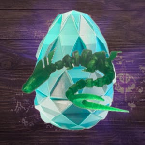 Op de afbeelding: Een geometrisch, lichtblauw eivormig object met een groene, gesegmenteerde, draakachtige creatuur eromheen gewikkeld. Het ei heeft een facetontwerp en de draak heeft een getextureerd uiterlijk. De achtergrond is een donkere houtnerf.