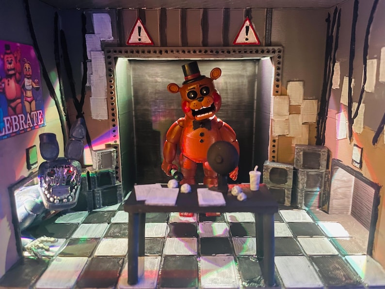 May include: A diorama featuring a brown bear animatronic figure with a black top hat and bowtie standing behind a black desk. The scene includes a chequered floor, a poster with the text CELEBRATE, two warning signs, and a detached animatronic head.