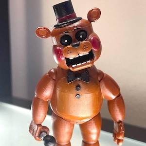 Op de afbeelding: Een bruine Freddy Fazbear actiefiguur met een zwarte hoge hoed, vlinderdas en microfoon. De figuur heeft rode wangen en een open mond. Dit is een verzamelobject uit de Five Nights at Freddy's videogame serie.