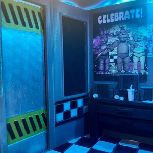 K&ouml;nnte beinhalten: Ein Miniatur-Raum-Diorama mit schwarz-wei&szlig;em Schachbrettboden, einem Wandplakat mit dem Text CELEBRATE! und drei animatronischen Figuren, einem Schreibtisch mit kleinen elektronischen Monitoren und einer T&uuml;r mit gelb-schwarzen Warnstreifen.
