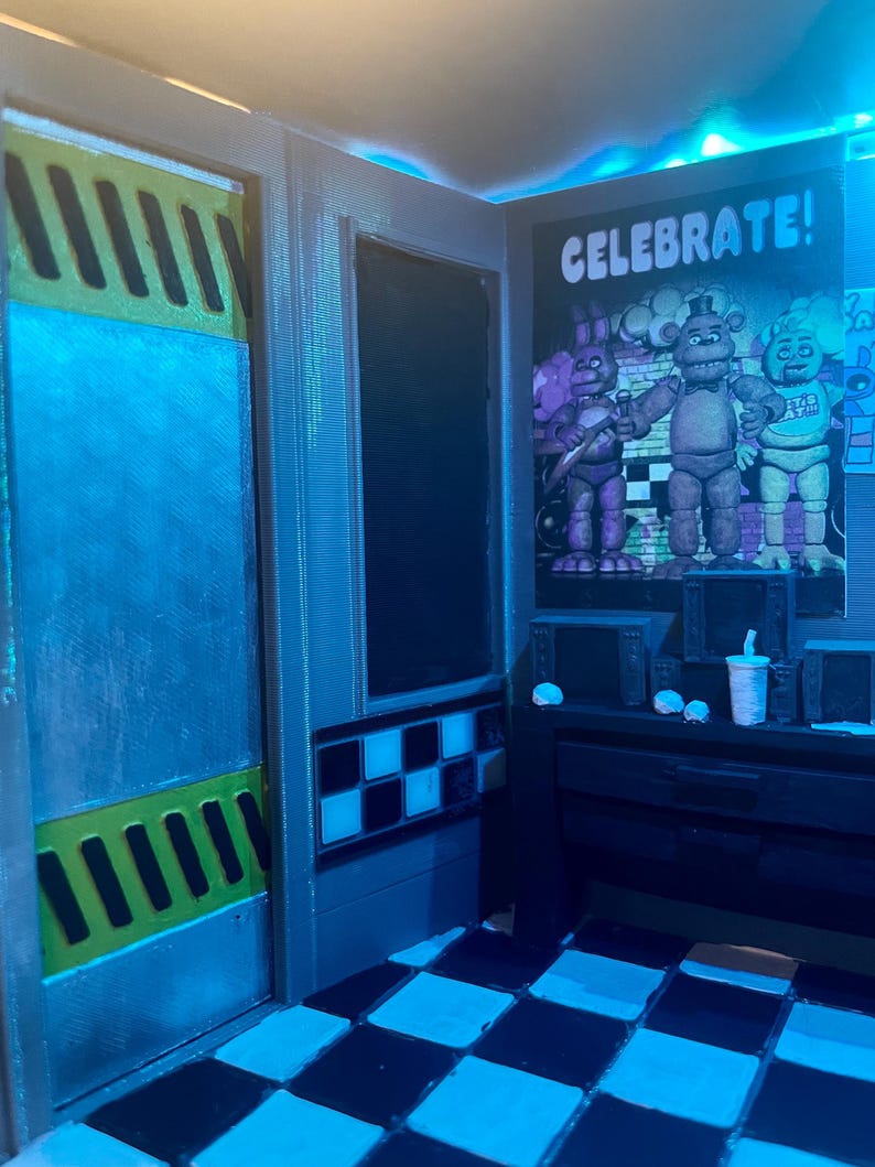 K&ouml;nnte beinhalten: Ein Miniatur-Raum-Diorama mit schwarz-wei&szlig;em Schachbrettboden, einem Wandplakat mit dem Text CELEBRATE! und drei animatronischen Figuren, einem Schreibtisch mit kleinen elektronischen Monitoren und einer T&uuml;r mit gelb-schwarzen Warnstreifen.