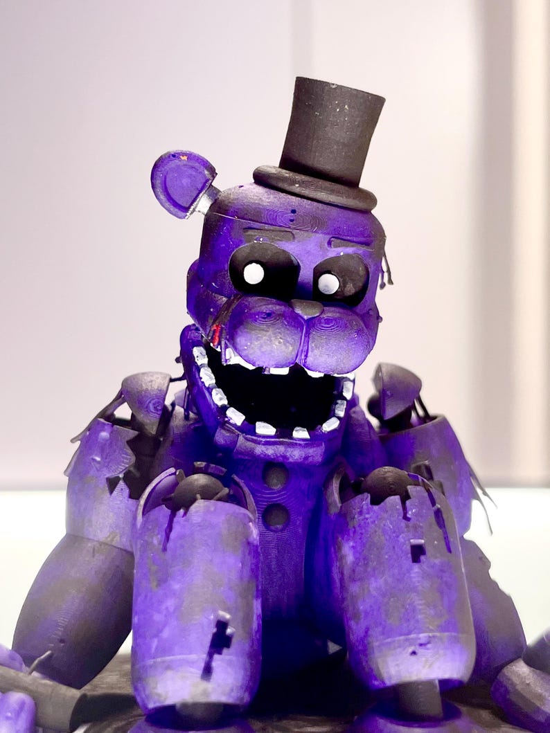 Puede incluir: Una figura morada con forma de oso con un sombrero de copa negro. La figura tiene la boca muy abierta, dientes visibles y una apariencia angustiada. El oso tiene da&ntilde;os y desgaste visibles.