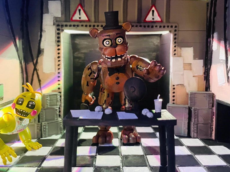 May include: A brown bear animatronic figure with a black top hat and bowtie stands behind a black desk. A yellow chicken animatronic figure is on the left. The scene features a black and white checkered floor, warning signs, and scattered papers.