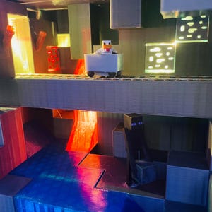 Puede incluir: Un diorama impreso en 3D con tem&aacute;tica de Minecraft con un pollo montando en un carro de mina, una cascada de lava y una figura negra de pie en una plataforma.