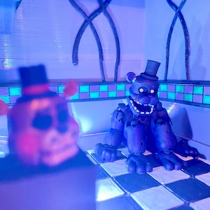 Op de afbeelding: Twee beerachtige figuren met hoge hoeden staan in een kamer met een geblokte vloer. E&eacute;n figuur staat onscherp op de voorgrond, terwijl de andere op de achtergrond staat, met een verweerd, donkerblauw uiterlijk en een open mond.